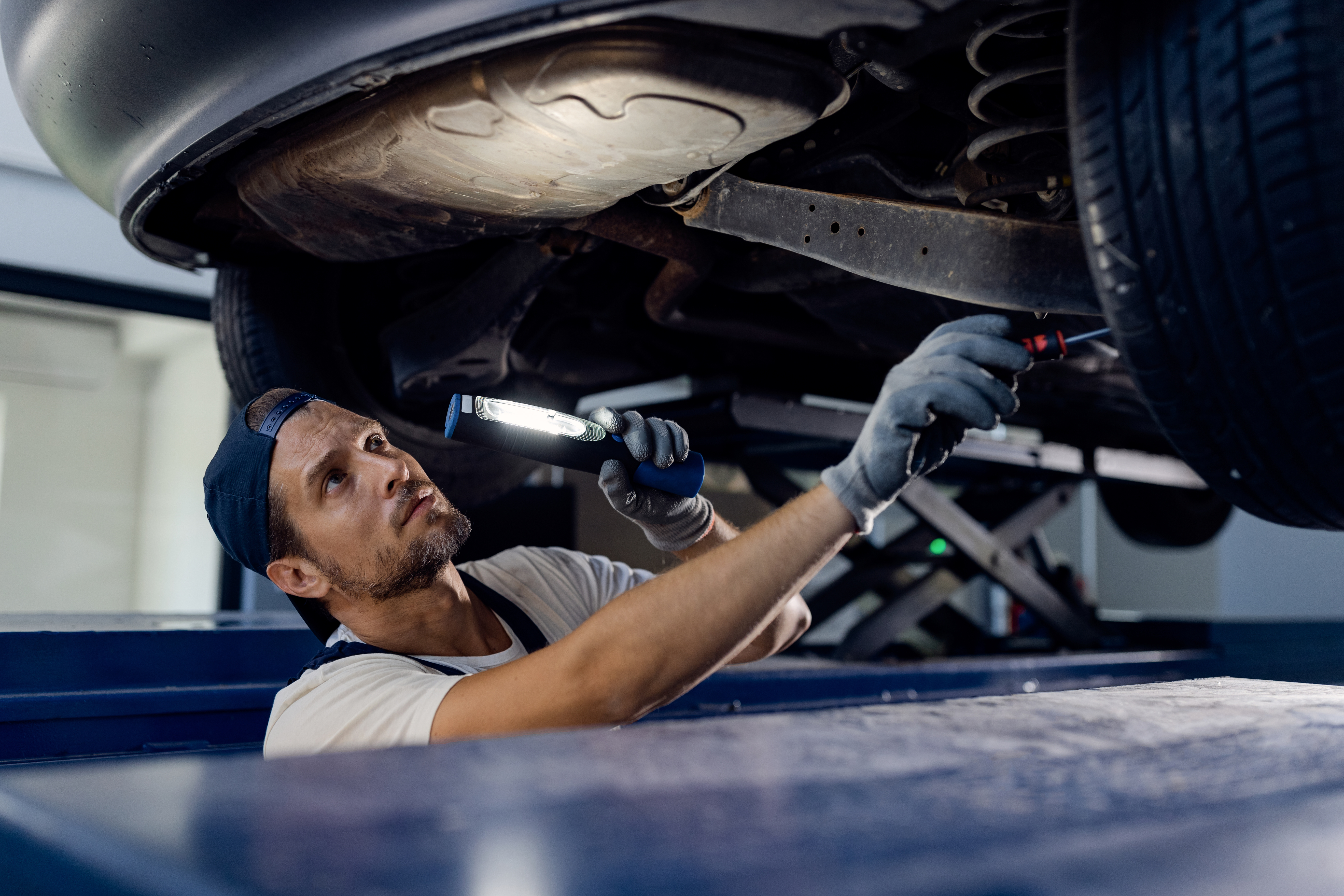 Automechaniker begutachtet ein Auto, das sich auf einer Hebebühne befindet, von unten