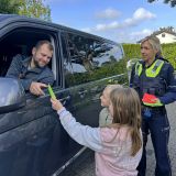 Zwei Kinder übergeben einem Autofahrer einen Dankzettel. Eine Polizistin steht daneben. 